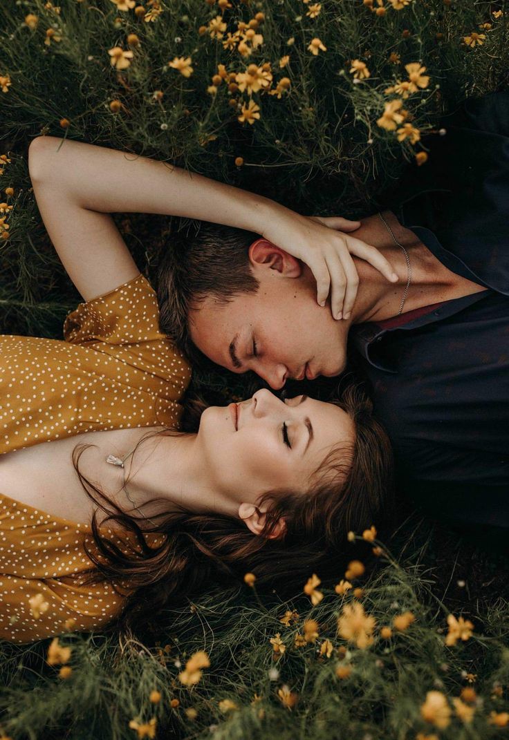 A young couple lying close together in a field of yellow wildflowers, gazing peacefully with eyes closed, creating a romantic and intimate moment.